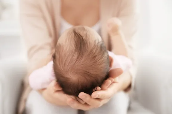 Mother holding cute baby on her knees closeup
